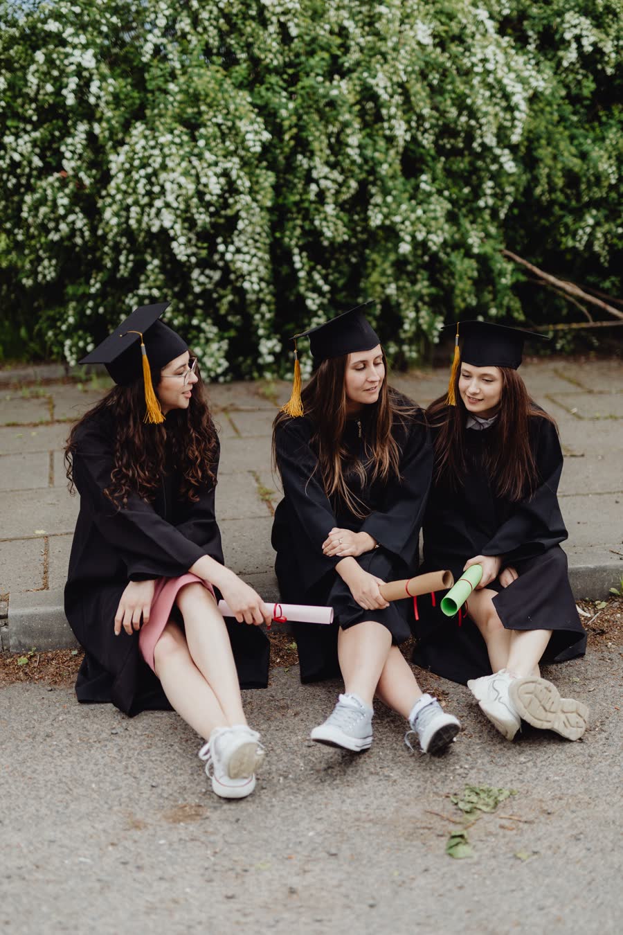 Three friends in gowns sitting together with their diplomas